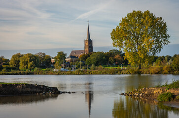 Obraz premium Church of Batenburg along the Meuse river next to old black poplar tree in the autumn