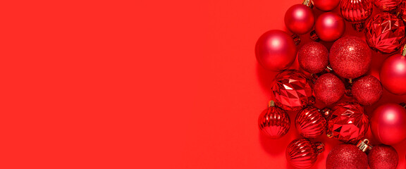 Beautiful red small decorative balls are scattered on a red background. Top view, flat lay. Banner.