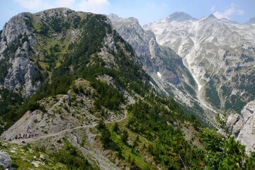 Fototapeta na wymiar Valbona Pass (Albanian: Qafa e Valbones) on trail from Theth Valley to Valbona Valley in Albanian Alps. Sihouettes of tourists on pass. It is one of the most beautiful high mountain trails.