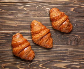 Top view of three French croissants arranged diagonally on a wooden background.