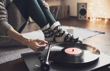 Young woman listening to music, relaxing, enjoying life at home. Girl wearing warm winter clothes having fun. Turntable playing vinyl LP record. Leisure, music, hobby, lockdown, lifestyle concept