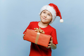 Merry Christmas. happy six-year-old kid in a Santa hat is holding a gift.
