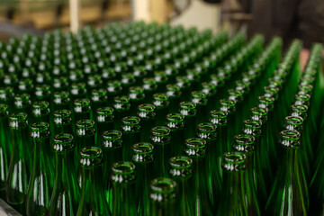 Fototapeta premium Glass factory, industrial production of glass containers. A lot of empty glass bottles as a background of green glass containers with copy space. Bottles for drinks. Technological work at the factory.
