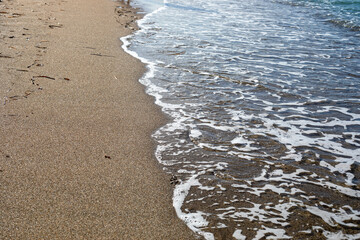 blurred sea background surf with foam on sandy beach top view, horizontal