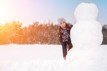 Cute girl makes a snowman on a winter day. A girl on a snow-covered field in the open air. Artistically colored and tinted photography