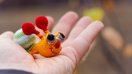 Textile handmade funny happy snail toy in hand on natural blurry background. macro photo. multi-colored snail. beautiful toy, close-up. the concept of childhood, games, education