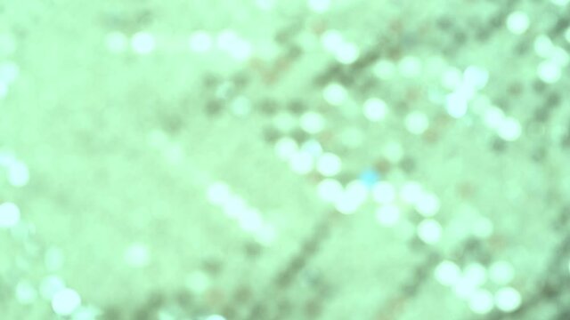 green texture of sparkling sequins on light fabric, background colored blur bokeh, round, defocused abstract christmas, wedding wallpaper, basis for designer