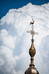Flèche du clocher d'une église composée d'une croix et d'un coq, sur un fond de nuage © Cyrille Voirol