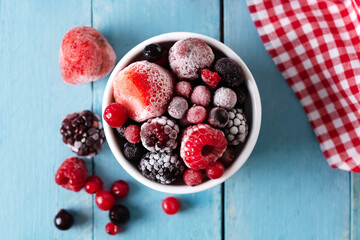 Assortment of iced berries in a bowl on blue wooden table. Top view