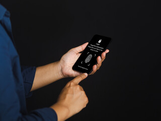 Young man scanning fingerprint biometric identity and approval on a smartphone while standing on a gray background. Business technology safety internet and biometric security Concept