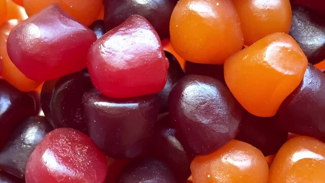 Close-up texture of red, orange and purple multivitamin gummies on white background. Healthy lifestyle concept
