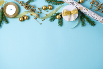 Christmas gold decorations with fir branch, gift box, ribbon on a light blue background. Holiday and celebration concept for postcard or invitation. Top view. Copy space