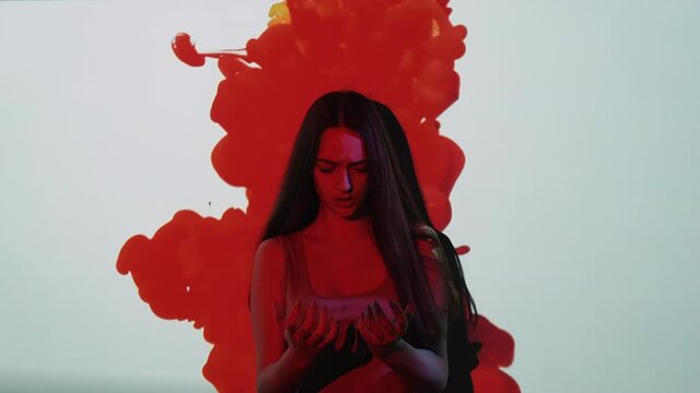 Murder horror. Creepy nightmare. Paranormal mystery. Terrified scared anxious psycho killer girl looking at hands in red blood drip on white wall copy space background.