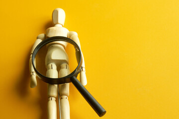 A wooden model of a man lies under a magnifying glass on a yellow background. The concept of gender...