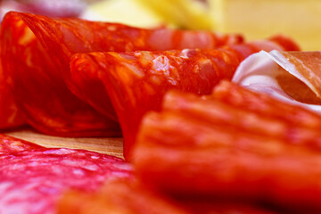 Focus on a wooden board sliced salami and cabanos sticks. Shallow depth of field. Wine appetizer.