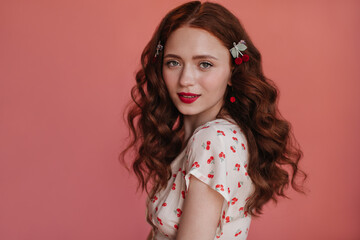 Close-up of fair-skinned girl with bright red lips looking at camera against pink background. Young...