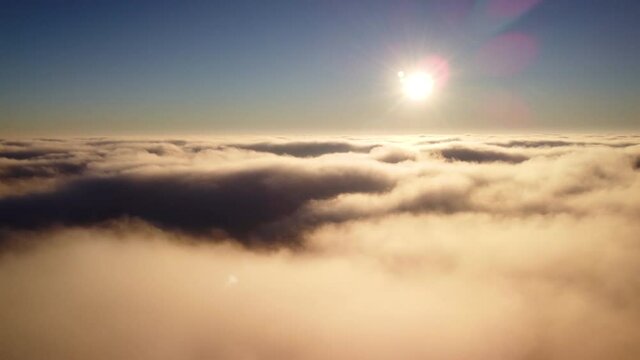 Airplane view in the sky, white fluffy clouds up in the sky, floating slowly. Setting sun over a layer of clouds