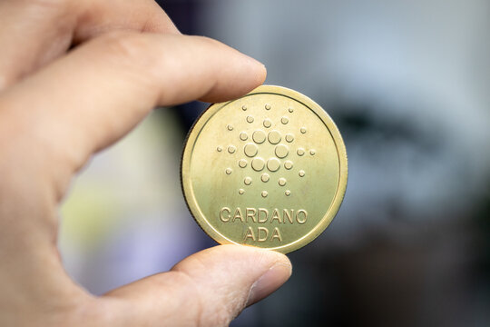 Cardano Ada coin held between two fingers