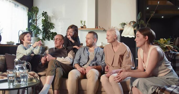 Multi generation family unity. Happy cheerful old grandparents, young dad and mom, teen boy and girl talk at living room