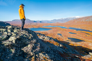 Male hiker overlooking epic view of vast arctic landscape of Stora Sjofallet National Park, Sweden,...
