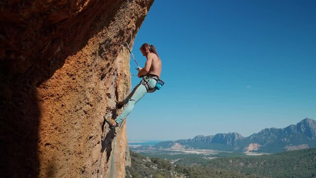 Young fit muscular attractive man rock climbing outdoors, preparing to rappel on rock face after successful climbing