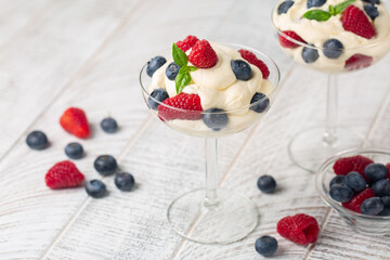 Mascarpone whipped cream with fresh berries. White wood table.