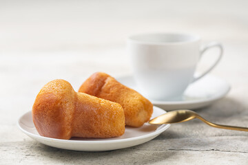 Rum baba or baba au rhum. Small yeast cake saturated in syrup made with rum.  Close-up, selective focus. Coffee cup. Light background.