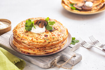 Savory thick crepes made of mashed potato, with fried mushrooms and sour cream. Light background.