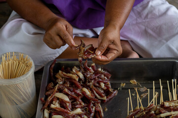 Hands of a merchant plugging the beef into the wood sticks to make grilled beef prepare for sale.