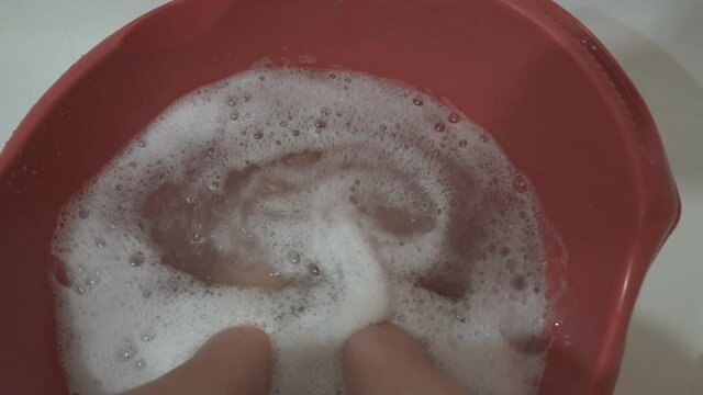 Woman bare feet in soapy water at home in bathroom. Slow motion.