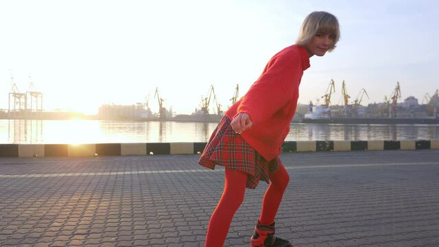 Stylish teenage girl rollerskating at sunrise, urban sports, fun leisure activity in sea port, teenage lifestyle