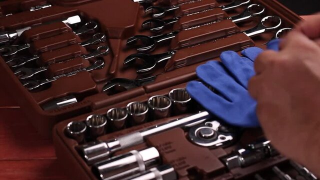 The foreman puts on work gloves and takes a wrench from a set of tools for repairing a car or motorcycle.