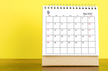 September 2022 desk calendar with yellow background on the wooden table.