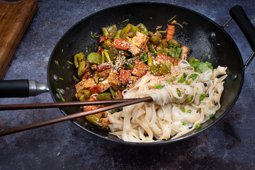 Vegan, gluten free tofu, carrot, pepper stir fry and noodles in wok with chiopsticks