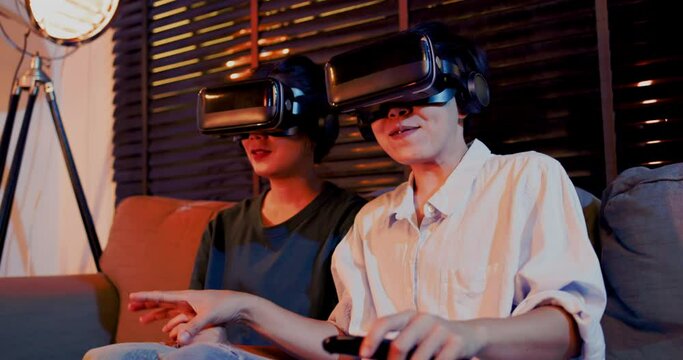 Asian couples wearing modern Virtual reality glasses sit and watch movies in living room at home. Holiday Activity family entertainment technology. living together happiness. Concept metaverse