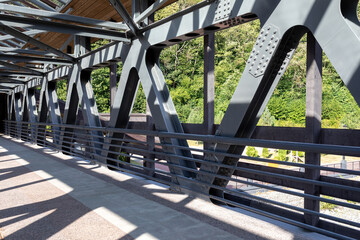 Pedestrian crossing over a river or highway. Covered bridge across the road. Bridge beams made of...
