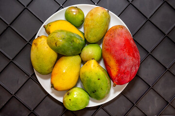 Typical varieties of Brazilian fruit Mango sword, coquinho, caipira and palmer, on white plate on dark background in top view