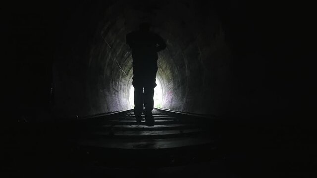 Slow motion video of man running in dark spooky tunnel toward bright light at end of passage way. Freedom and hope concept video background