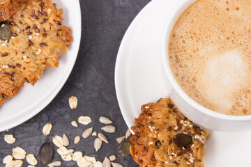 Cup of coffee with milk and fresh baked oatmeal cookies on white plate. Delicious crunchy dessert