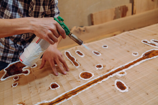 Carpenter removing air bubbles with blowtorch from epoxy table