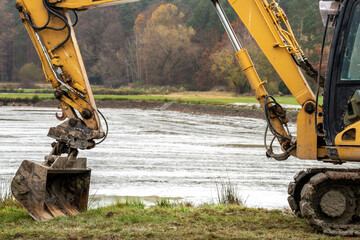 A yellow excavator in front of a muddy pond