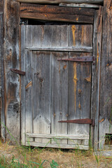 The closed door of an old barn made of planks. Darkened boards. Rusty hinges. There is no lock. Soft light.