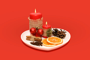 White plate with a red candle and dried oranges and a pine cone.