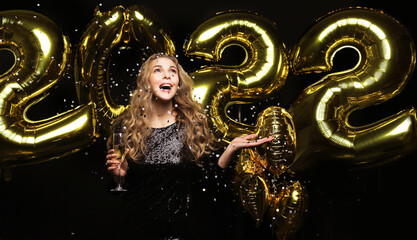 Happy gorgeous girl in stylish sexy party dress holding gold 2022 balloons, having fun at Christmas or New Year's Eve Party.