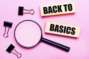 On a pink background, a magnifier, black paper clips and wooden blocks with the text BACK TO...