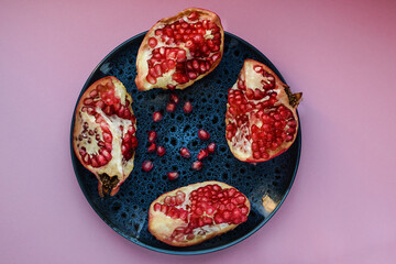 Ripe pomegranate fruits on a dark plate, on a colored background. Healthy eating. Top view.