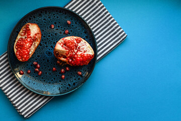 Two pieces of pomegranate on a blue plate, kitchen cotton napkin on a blue background. Food...