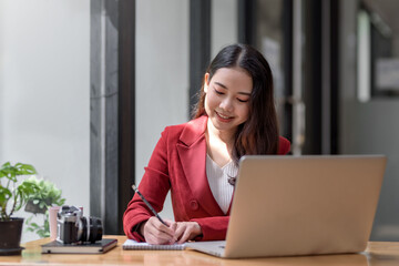 Smiling young Asian businesswoman is happy to work at the modern office using a laptop computer.