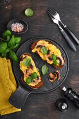 Scrambled eggs with fried mushrooms and basil on bread on black table background. Homemade breakfast or brunch meal - scrambled eggs and mushrooms sandwiches. Top view with copy space