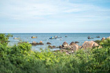 Fototapeta na wymiar Scenic view of the beach with big stones. Boats is sailing on the sea. View of the bay with crystal water. Colourful vietnamese fishing boats.